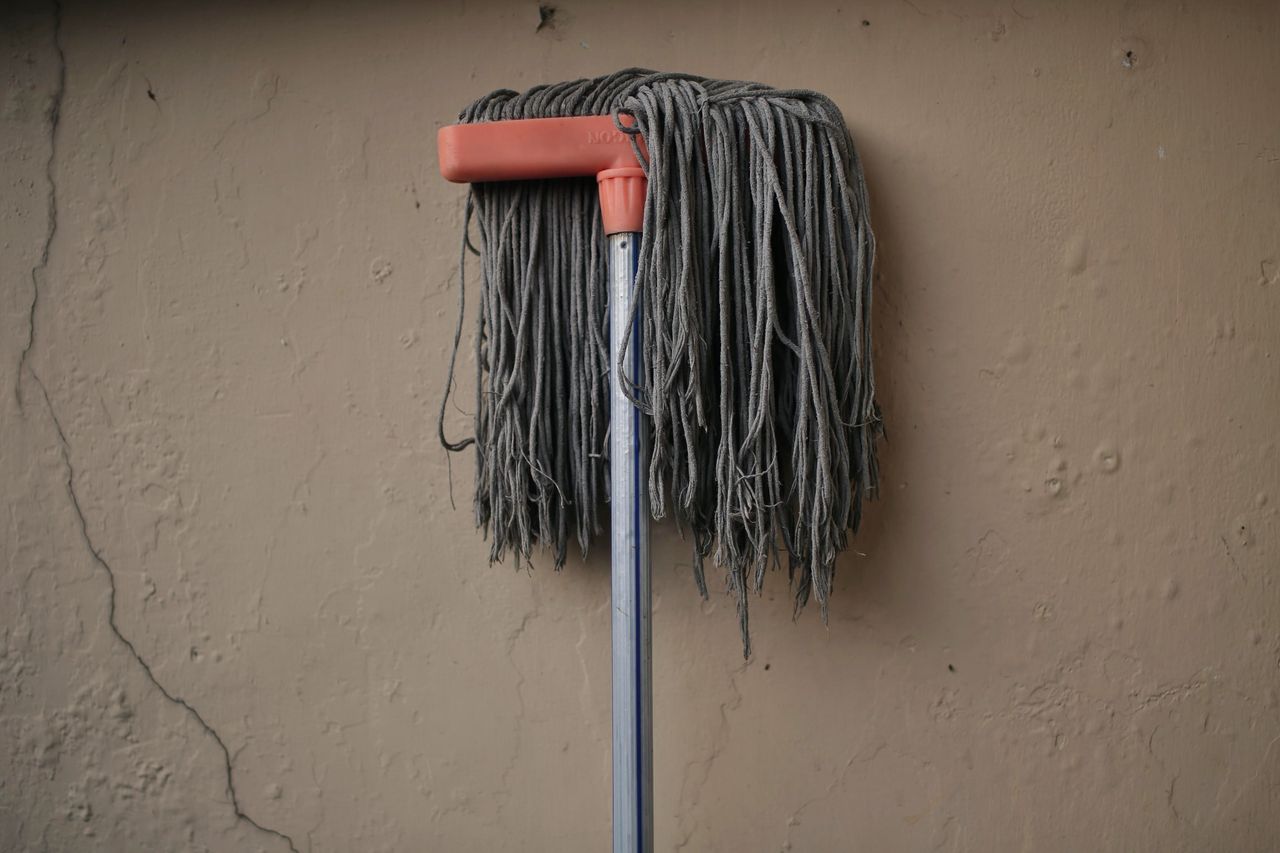 Gray mop leaning against a textured wall, conveying simplicity in a domestic setting.